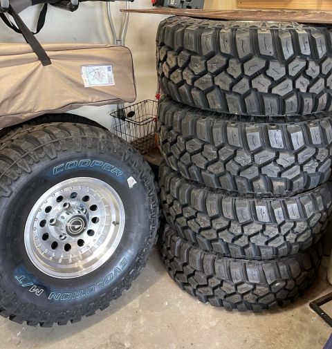 1984 Ford Bronco - A stack of four off-road tires sits next to a single Cooper Evolution M/T tire mounted on a polished aluminum wheel.