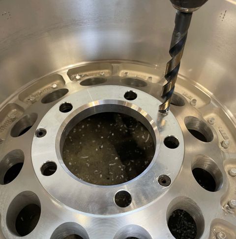 1984 Ford Bronco - A drill bit is shown in action, creating a new hole in a silver alloy wheel. The wheel has multiple lug nut holes and a polished finish.