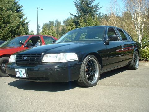 1999 Ford Crown Victoria - A black Ford Crown Victoria is parked outside, with another car visible in the background.