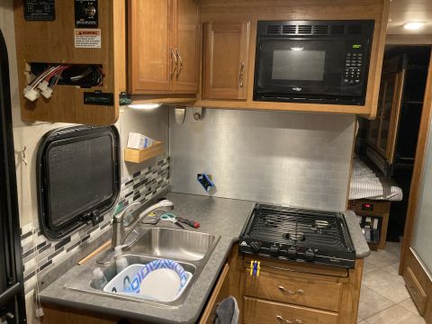 2015 Ford F-550 - Interior view of an RV kitchen a sink, stovetop, and microwave, with cabinetry and a window visible.