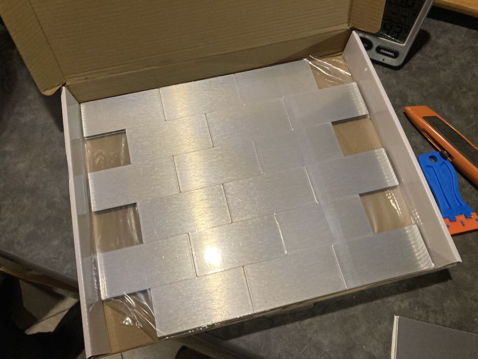 Box of brushed aluminum backsplash tiles, some with protective plastic