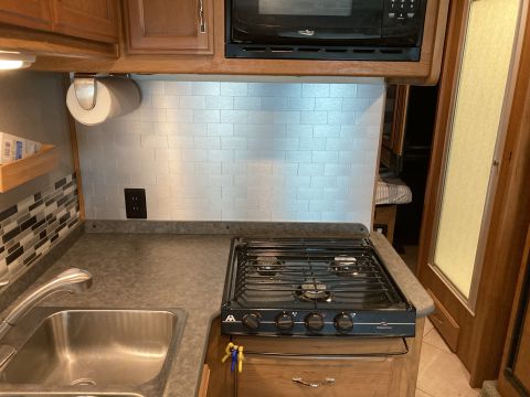 2015 Ford F-550 - Interior view of an RV kitchenette showing a sink, four-burner stovetop, and microwave above a tiled backsplash.