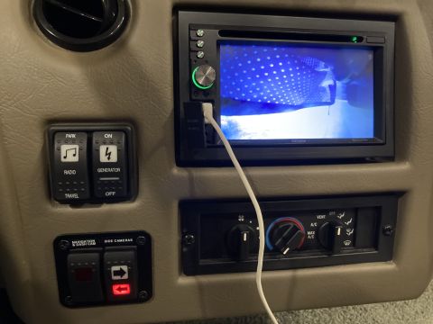 2015 Ford F-550 - Interior view of dashboard controls including radio, generator, and camera switches, along with climate control knobs and a screen.