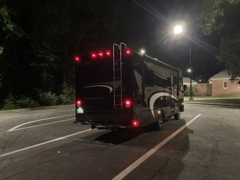 2015 Ford F-550 - A black motorhome is parked at night, showing its rear lights and ladder.