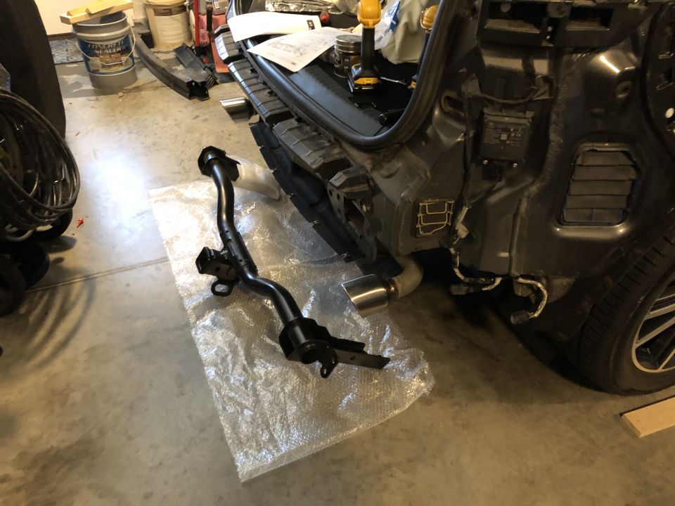 Vehicle rear bumper assembly removed, with a tow hitch receiver laid out on plastic wrap