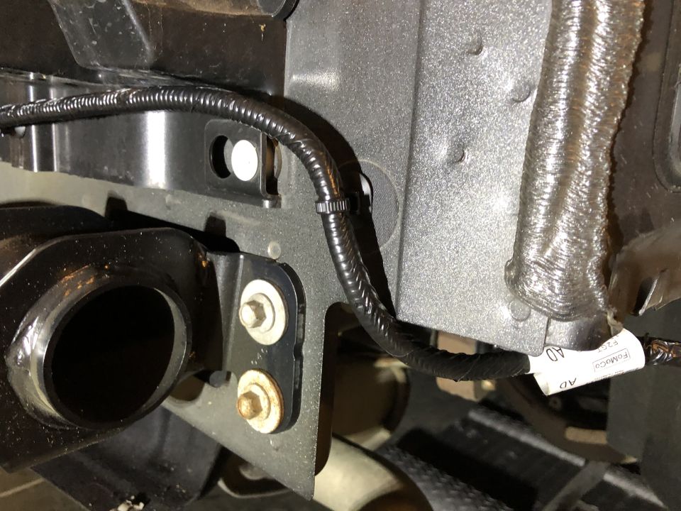 Close-up of a tow hitch wiring harness with black protective tubing and zip ties. A white label with text is visible