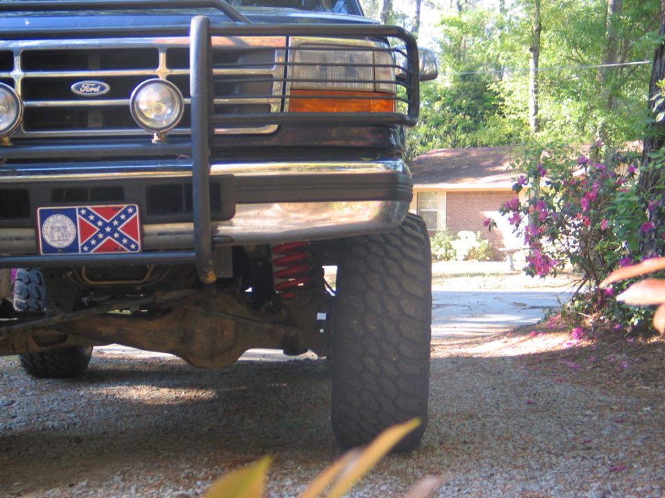 Front view of a dark-colored Ford Bronco with a chrome bumper, bull bar, and aftermarket lights. A Confederate flag license plate is visible
