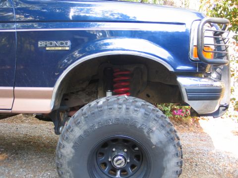 1995 Ford Bronco - Close-up view of the front fender, wheel, and suspension of a blue Ford Bronco.