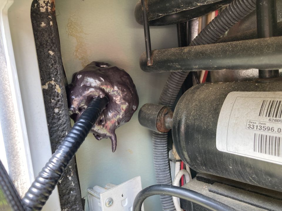 Melted sealant around a black wire conduit with a compressor unit visible