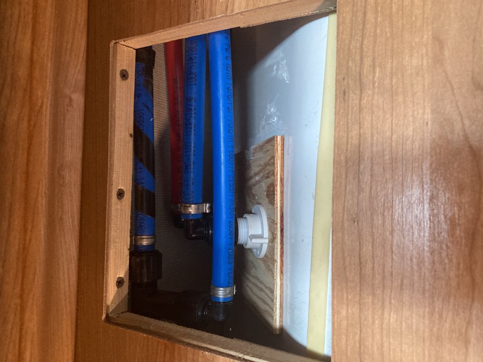 RV plumbing access panel showing hot and cold water lines and a white fitting
