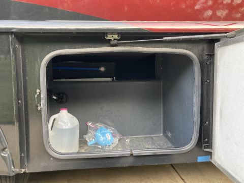 2015 Ford F-550 - RV storage compartment holds a water jug and a blue funnel.
