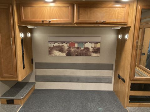 2015 Ford F-550 - The interior of an RV shows a bed area with overhead cabinets and a decorative painting of beach huts.