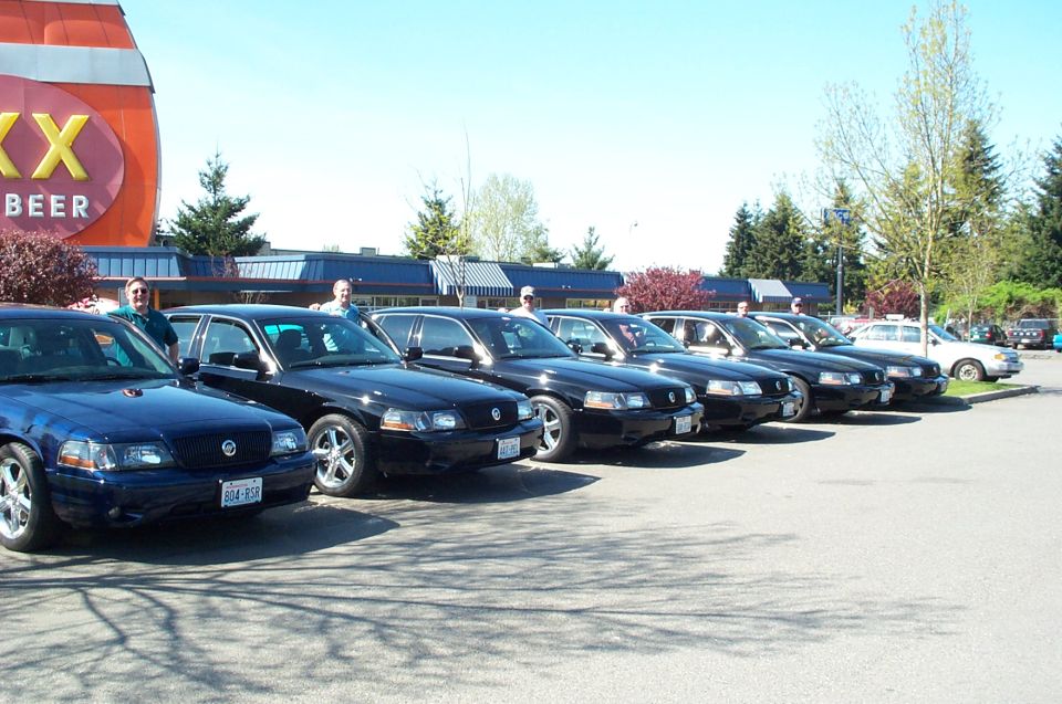 Row of dark blue and black full-size sedans lined up in a parking lot near a large beer barrel sign.