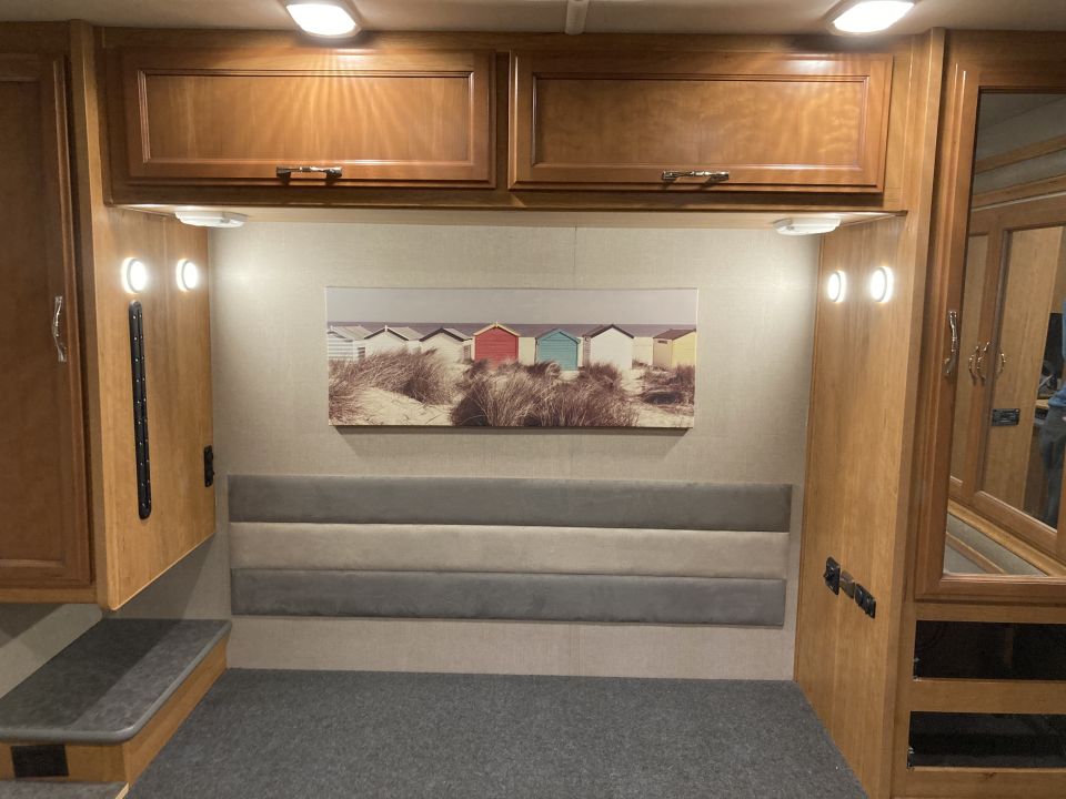 RV interior with wood cabinets, upholstered headboard, and beach hut artwork