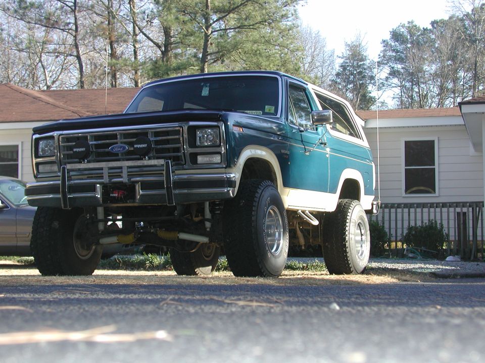 Lifted teal-and-white Ford Bronco with brush bar and twin driving lights, low front three-quarter view