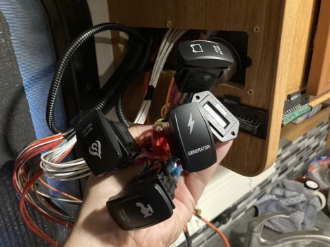 2015 Ford F-550 - A hand holds various electrical switches, including ones labeled 'GENERATOR' and 'WATER HEATER', in a panel.
