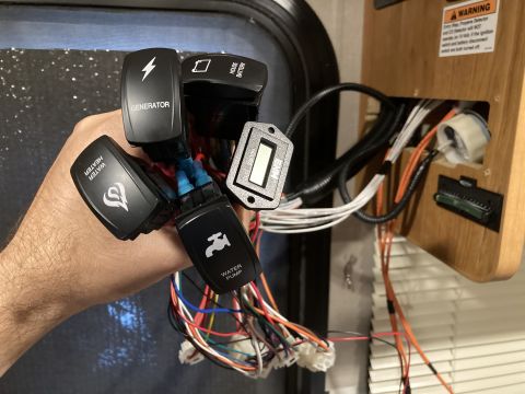 2015 Ford F-550 - A hand holds a monitor panel with various switches and wiring, including controls for generator, water heater, house battery, and water pum…