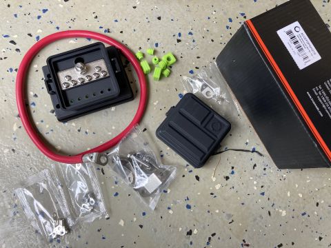 2015 Ford F-550 - A 12 volt bus bar kit is laid out on a speckled floor, including a red cable, green protective caps, and various hardware pieces.