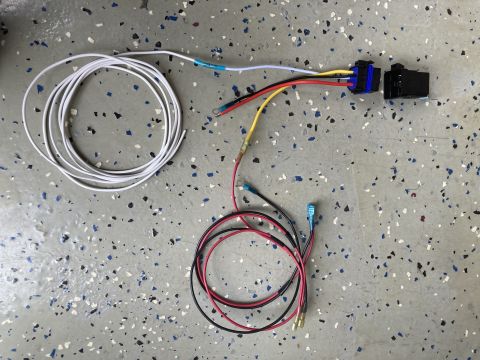 2015 Ford F-550 - A wiring harness with a relay and multiple colored wires, including white, red, and yellow, is laid out on a speckled floor.
