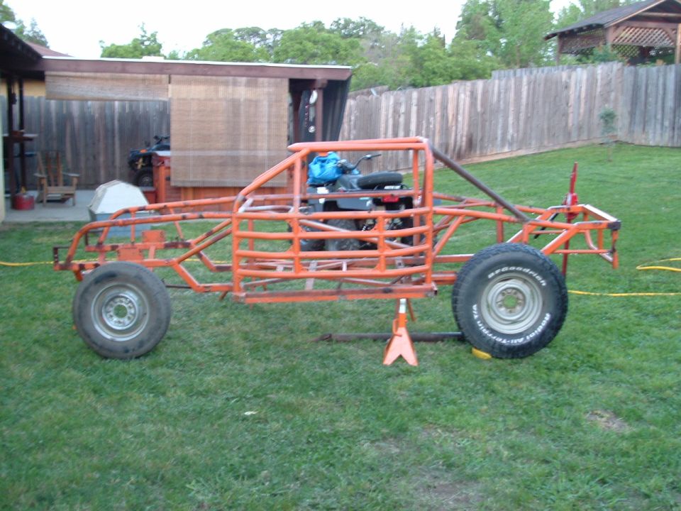 Orange tubular race car chassis on grass, with an ATV inside the frame