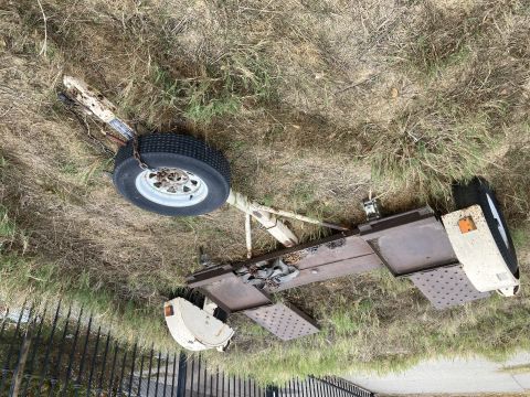 2015 Ford F-550 - A rusty tow dolly sits on the grass, showing its single wheel and metal deck.
