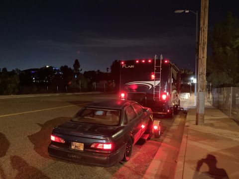 2015 Ford F-550 - An RV tows a dark sedan on a dolly at night, with the RV's brake lights illuminated.