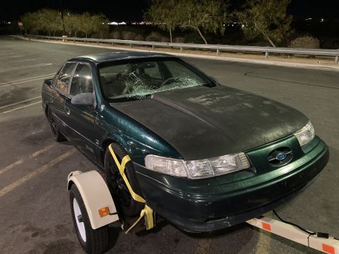 2015 Ford F-550 - A green sedan with a cracked windshield is loaded onto a tow dolly at night.