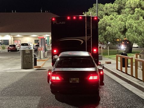 2015 Ford F-550 - A car is being towed by a large RV at a gas station. The RV has 'FLAIR' written on the back.