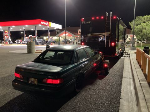 2015 Ford F-550 - A dark green sedan is towed by a large RV trailer at a gas station.