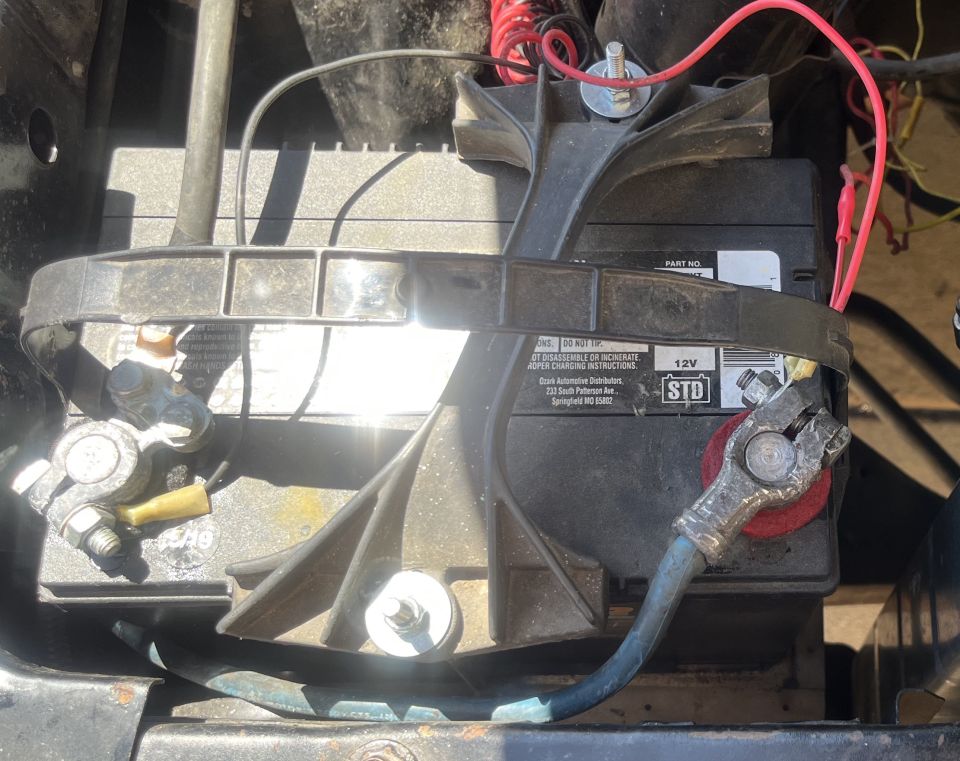 Car battery with red and blue cables connected to terminals. Battery has warning labels and 'STD 12V' marking