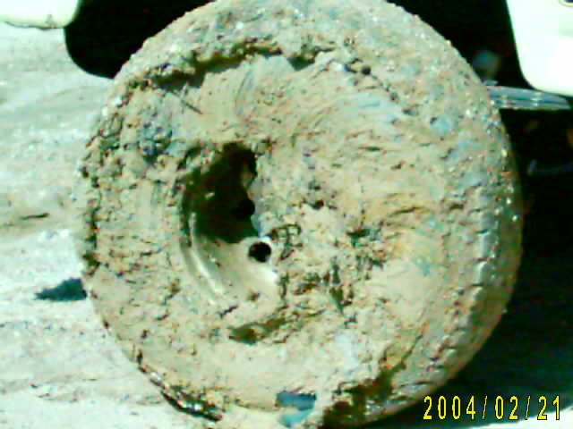 Mud-covered tire and wheel, with part of a white vehicle visible