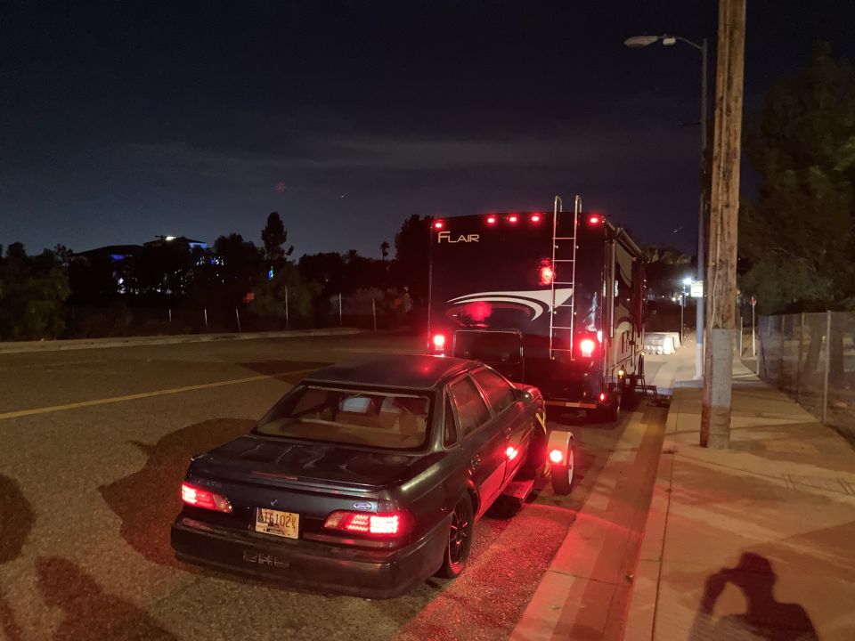 Dark sedan with license plate AFE102 towing a black RV at night