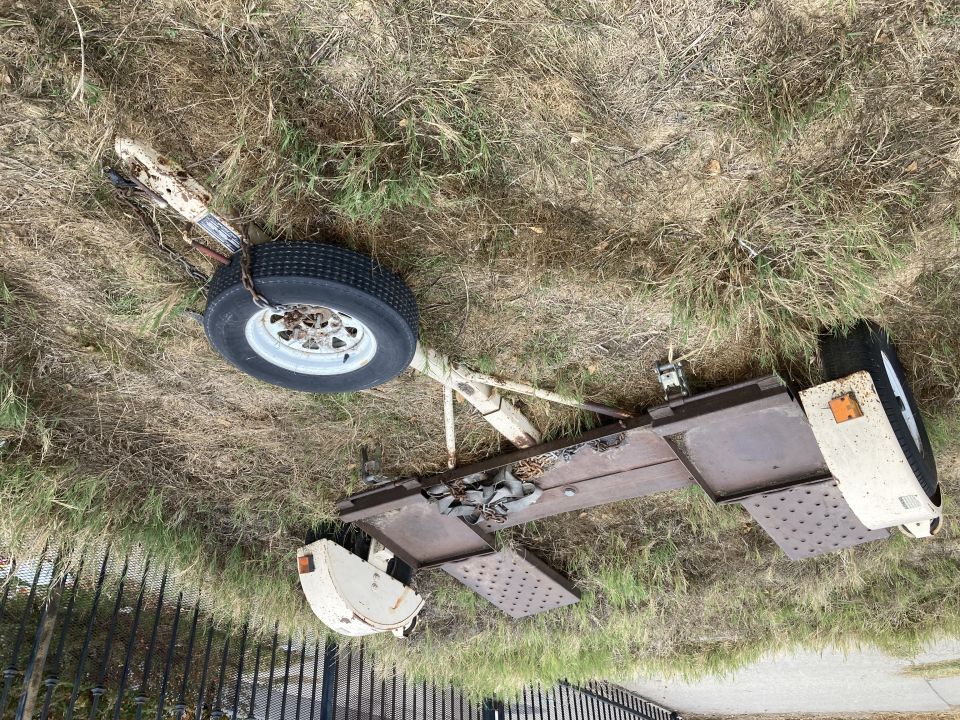 Car trailer frame with one wheel, jack, and chains on grassy ground