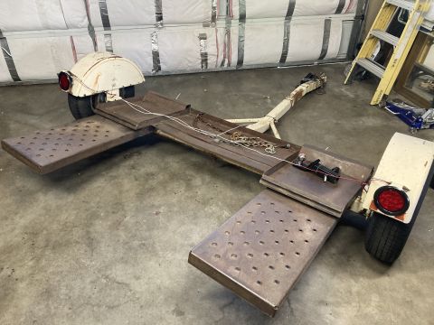 2015 Ford F-550 - A white car tow dolly with metal ramps and chains is shown on a concrete floor.