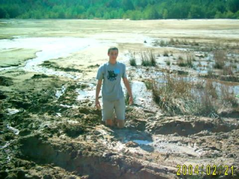 1985 Ford Bronco - A person is stuck in a muddy area with vegetation and water surrounding them.