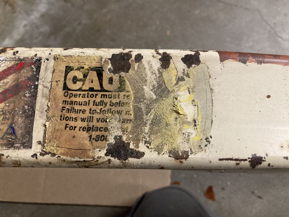 Close-up of a worn sticker with 'CAUTION' and instructions on a white metal surface with rust