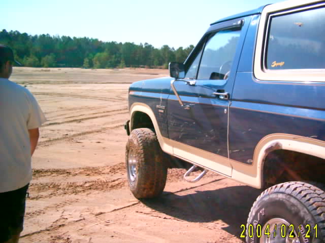 Blue and white 1985 Ford Bronco side view on sandy ground