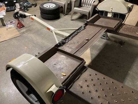 2015 Ford F-550 - A trailer with a cream-colored fender and wheel is shown, a rusty metal deck and chains. Tools and chairs are visible in the background.