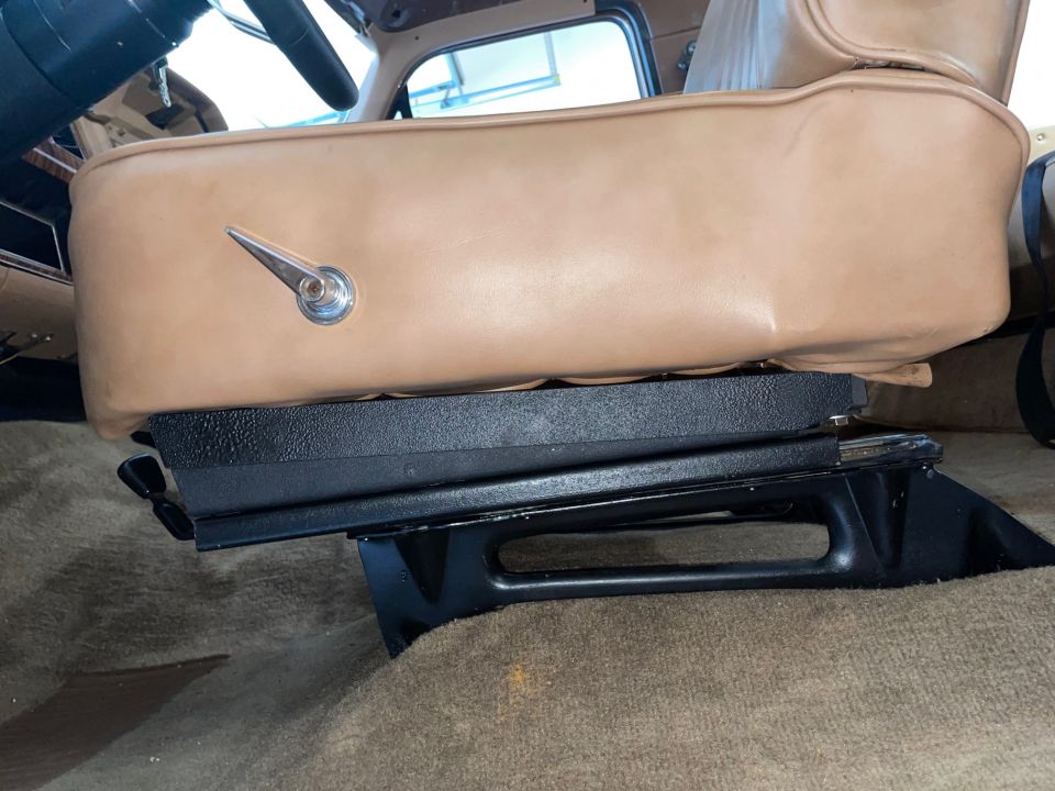 Close-up of a tan seat with a chrome adjustment lever and black seat base