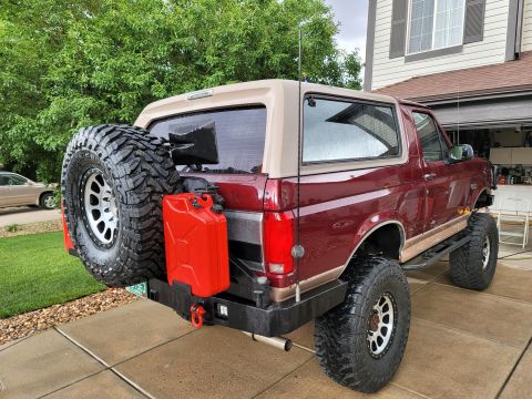 1996 Ford Bronco - Rear view of a red and tan 1996 Ford Bronco, equipped with a spare tire and a red jerrycan on the custom bumper.