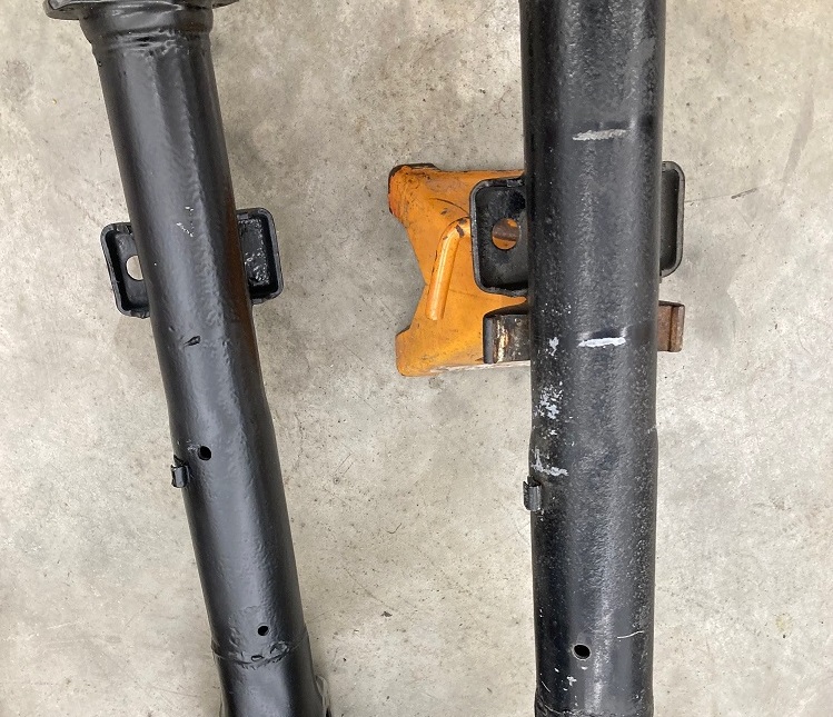 Two black metal axle housing tubes with orange metal bracket in between