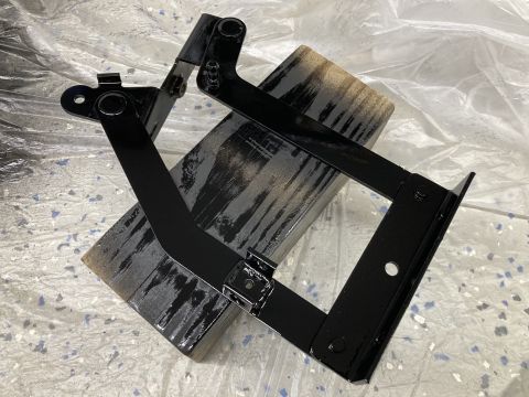 2015 Ford F-550 - These are hood brackets, likely for a vehicle, that have been painted black and are resting on a wooden block.