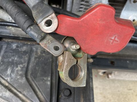 2015 Ford F-550 - A close-up view of a vehicle's battery terminal, showing the red positive cover and a metal clamp attached to the cable.