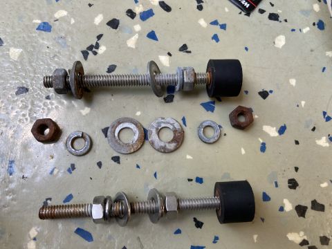 2015 Ford F-550 - Two metal hood brackets with rubber bumpers and assorted nuts and washers are laid out on a speckled surface.