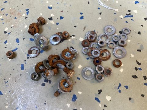 2015 Ford F-550 - A collection of assorted bolts, nuts, and washers, many showing signs of rust, are scattered on a floor with blue and black flecks.