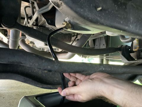 2015 Ford F-550 - hand guiding a black hose through the undercarriage of a vehicle, with suspension links, frame, and an oil filter visible above.