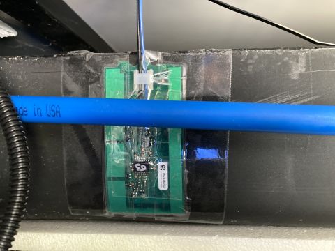 2015 Ford F-550 - A close-up shows a circuit board attached to a black surface, with a blue pipe passing over it.