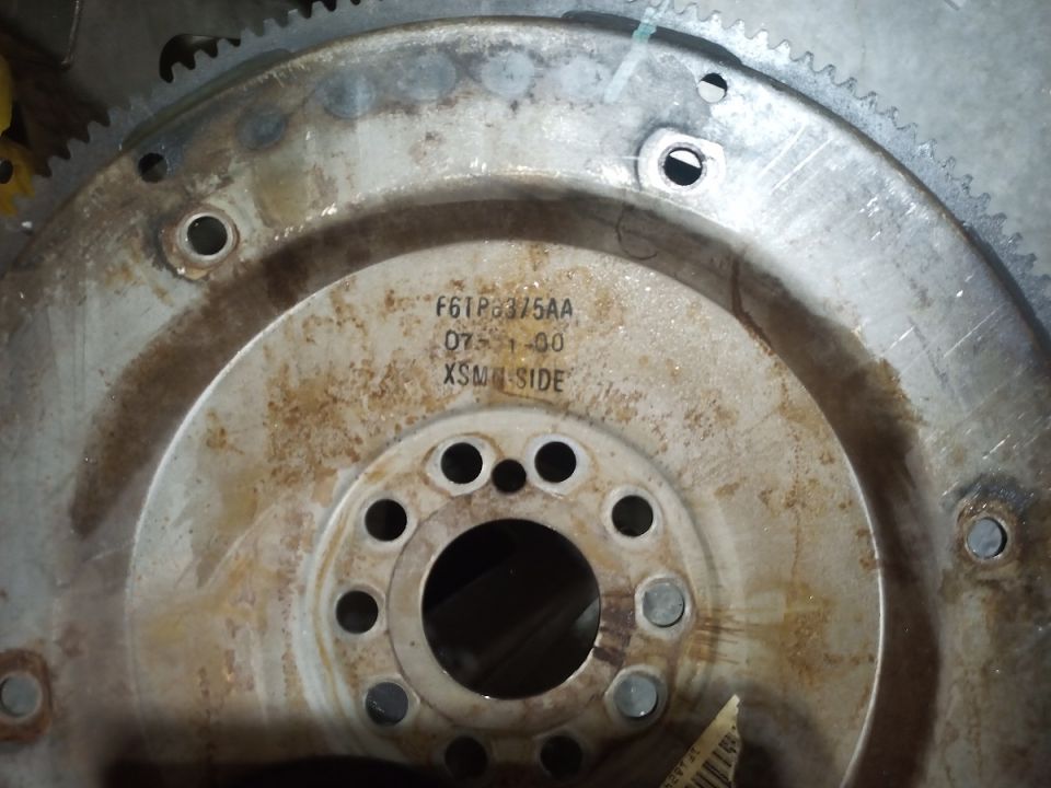 Close-up of a rusty metal flywheel with part numbers stamped on it
