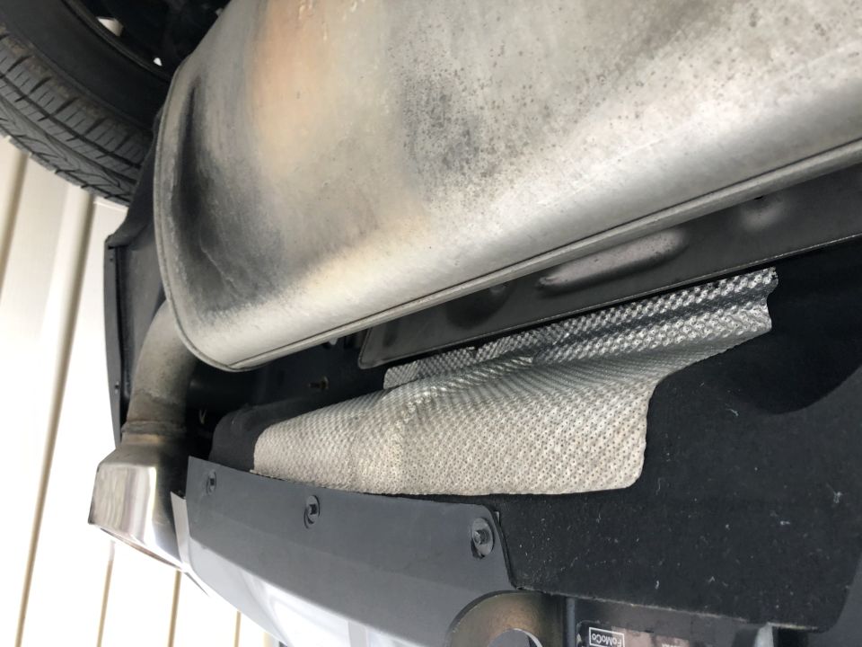 Underside view of a vehicle's exhaust pipe, muffler, and tow hitch receiver. Text reads SUPERMOTORS.NET