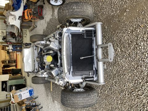 1976 Chevrolet Corvette - The chassis of a Chevrolet Corvette is shown with its engine and radiator exposed, resting on tires in a gravel-floored garage.